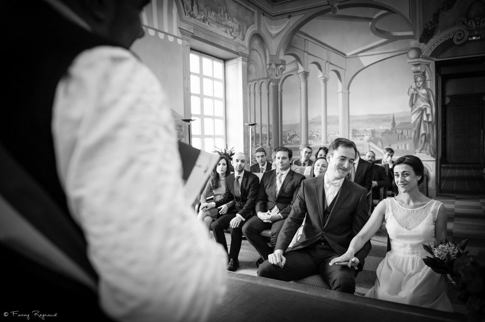 Mariage civil à la mairie de clermont-ferrand dans le puy-de-dome (63). Les mariés regardent le maire qui lit l'acte de mariage et sourit de bonheur.