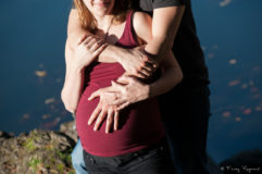 Photographie d'une femme enceinte avec son compagnon au lac de la cassière en auvergne, détails sur le ventre et les mains. Cadrage coupé au sourire de la future maman. Séance de photographie en extérieur par fanny reynaud photographe professionnelle à clermont-ferrand.