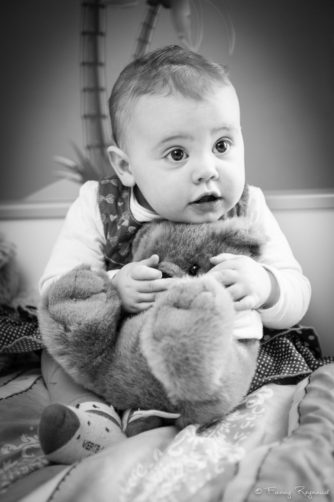 Photo d'une petite fille avec un gros ours en peluche, en noir et blanc et en lumière naturelle, réalisée lors d'un shooting à domicile près de clermont-ferrand par un photographe professionnel. © Fanny Reynaud.