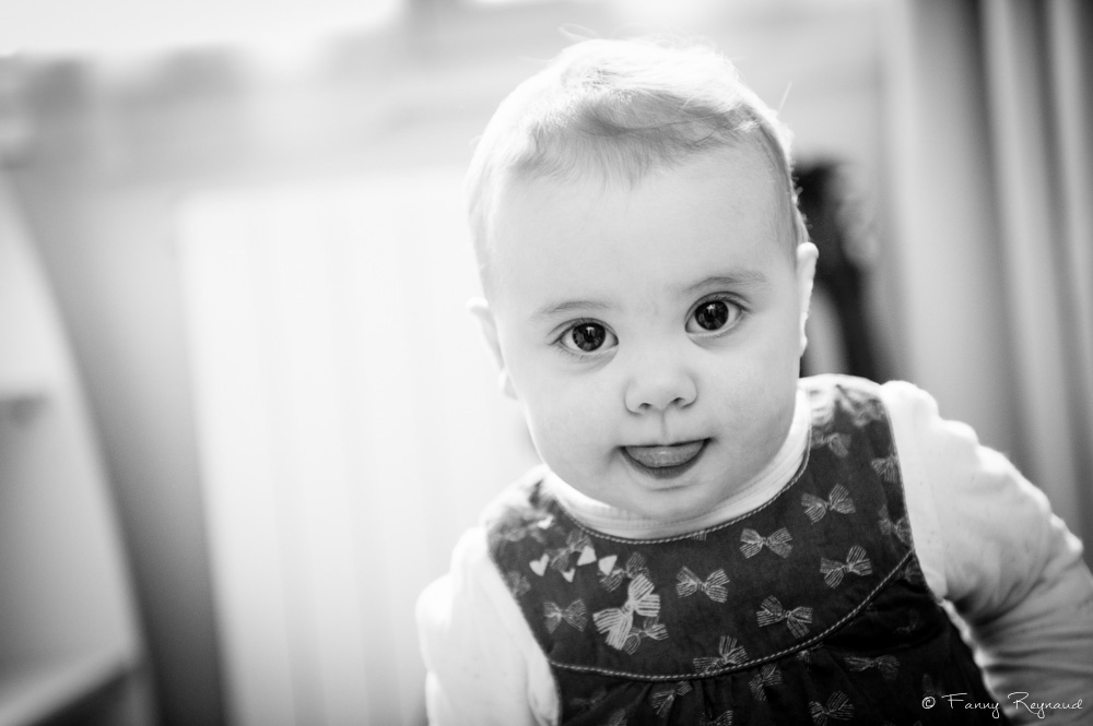 Photographie d'une petite fille de deux ans en noir et blanc qui nous offre un beau regard. © Fanny Reynaud photographe à domicile dans le puy-de-dome pour séance photo de famille chez vous.
