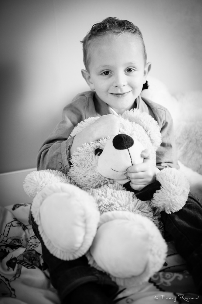 Portrait d'un petit garçon avec une de ses peluches, un nounours. Photo noir et blanc en lumière naturelle réalisée pendant une séance à domicile à volvic, près de clermont-ferrant et riom dans le puy-de-dome (63).